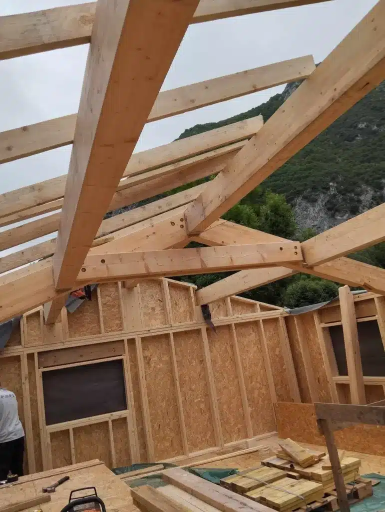 Charpente en bois traditionnelle en cours de construction, illustrant le travail minutieux d'un charpentier avec des poutres robustes, adaptées à une structure de maison en bois située dans une région montagneuse.