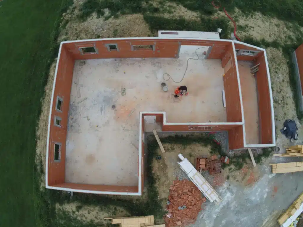 Vue aérienne des fondations et des murs d'une maison en cours de construction, illustrant la réalisation des murs et des cloisons par une entreprise de maçonnerie générale.