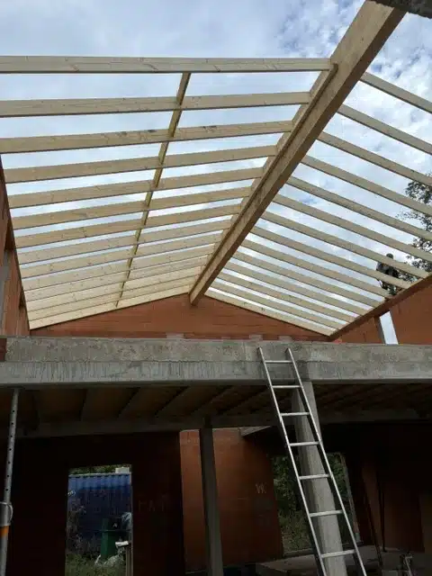 Charpente installée sur des murs porteurs en béton, représentant une étape avancée d'un projet de construction, réalisée par des experts en maçonnerie générale et charpenterie.