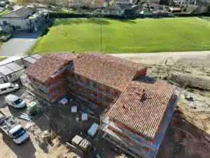 Vue aérienne d'un chantier de construction de maisons avec des toitures en tuiles traditionnelles dans un environnement verdoyant.