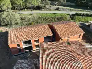 Vue aérienne d'un chantier de construction de maisons avec des toitures en tuiles traditionnelles dans un environnement verdoyant.