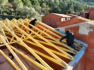 Construction de toiture en bois sur un bâtiment en briques, avec un ouvrier et un paysage naturel en arrière-plan.