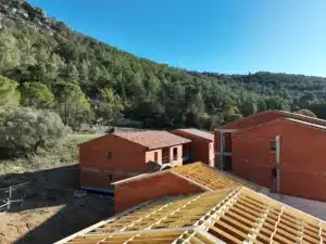 Vue aérienne d'un chantier de construction de maisons avec des toitures en tuiles traditionnelles dans un environnement verdoyant.